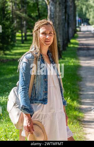 Eine junge Frau mit geflochtenen Haaren genießt einen sonnigen Spaziergang im Park und verkörpert einen ungezwungenen, unbeschwerten Sommertag Stockfoto