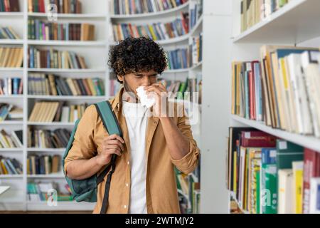 Ungesunder Mann in Casualwear mit Papierserviette beim Niesen und am Gang mit Romansammlung stehen. Kranker islamischer Mann, der im Buchladen mit Stauballergie kämpft, während er die Schultertasche hält. Stockfoto