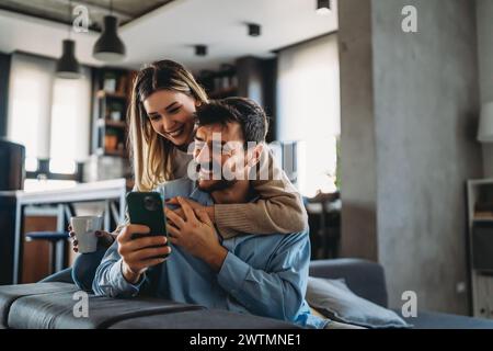 Ein junges glückliches Paar, das zu Hause Nachrichten aus sozialen Medien per Telefon mitteilt und online einkauft. Stockfoto