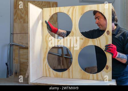 Ein hispanischer Zimmermann mittleren Alters, der in seiner Tischlerei steht und ein Möbelstück zusammenbaut Stockfoto