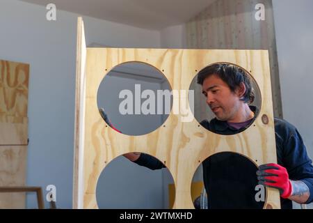 Ein hispanischer Zimmermann mittleren Alters, der in seiner Tischlerei steht und ein Möbelstück zusammenbaut Stockfoto