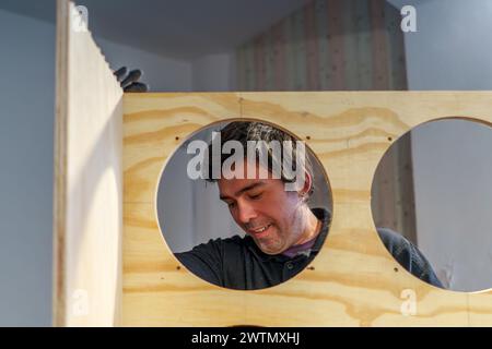 Ein hispanischer Zimmermann mittleren Alters, der in seiner Tischlerei steht und ein Möbelstück zusammenbaut Stockfoto