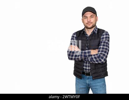 Erwachsener Mann in lässigem kariertem Hemd, Weste Bodywärmer und schwarzer Mütze, der mit überkreuzten Armen steht und in die Kamera blickt. Stockfoto