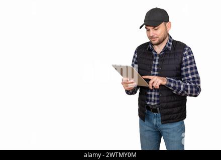Ein isolierter Mann, der legere Kleidung und eine Kappe trägt, verwendet ein digitales Tablet. Landwirt arbeitet mit digitalem Mobilgerät. Stockfoto