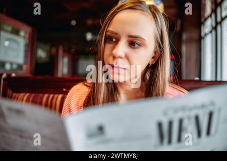 Eine Frau sitzt an einem Tisch und liest aufmerksam ein Menü Stockfoto