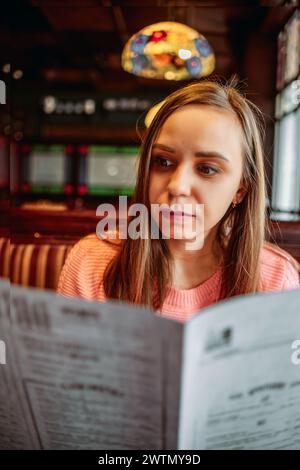 Eine Frau sitzt an einem Tisch und liest aufmerksam ein Menü Stockfoto