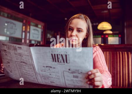 Eine Frau sitzt an einem Tisch und liest aufmerksam ein Menü Stockfoto