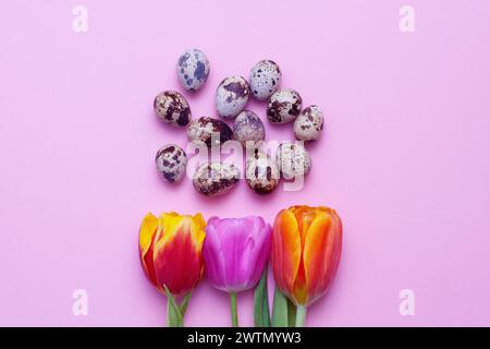 Ostereier Wachtelkomposition und rote Tulpen auf rosa Papierhintergrund. Stockfoto