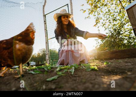 Eine Farmerin lächelt, die Freilandhühner auf dem sonnigen Bauernhof mit Grünfutter versorgt Stockfoto