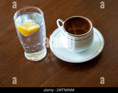 Türkischer Kaffee in klassischer Kaffeetasse und Wasser mit Zitrone auf Holztisch Stockfoto