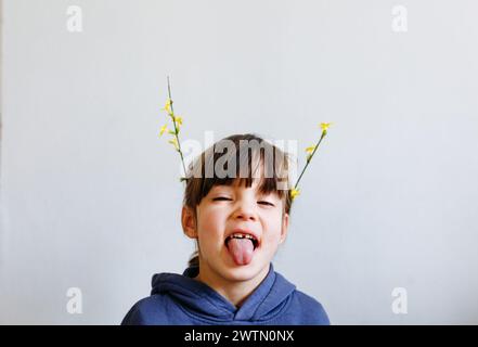 Porträt eines lächelnden kleinen Mädchens mit Blumen auf dem Kopf, die ihre Zunge zeigen Stockfoto