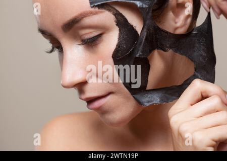 Eine schwarze Maske auf das Gesicht einer schönen Frau. Spa-Behandlungen und Katzenpflege im Schönheitssalon. Stockfoto