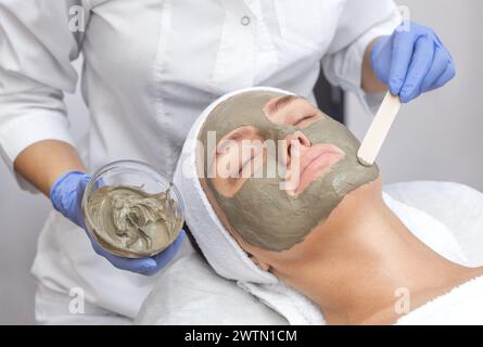 Das Verfahren zum Auftragen einer Maske aus Ton auf das Gesicht einer schönen Frau. Spa-Behandlungen und Katzenpflege im Schönheitssalon. Stockfoto