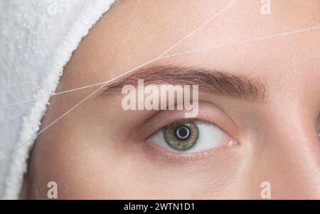 Die Make-up-Künstlerin zupft ihre Augenbrauen mit einer Fadennaht. Gesichtspflege, Schönheitsbehandlungen im Schönheitssalon. Stockfoto