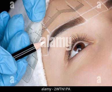 Permanent Make-up für Augenbrauen einer schönen Frau mit dicken Augenbrauen im Schönheitssalon. Nahaufnahme-Kosmetikerin, die Augenbrauen tätowiert. Stockfoto