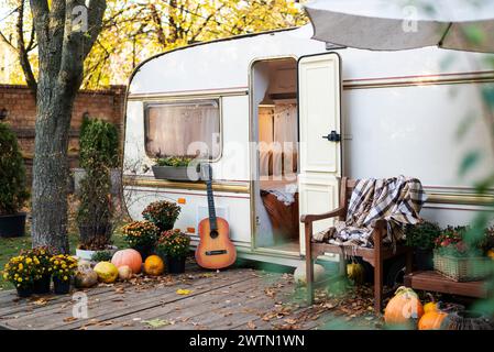 Wohnmobil mit Terrasse bei Sonnenuntergang im Herbst, Wohnmobil, orange gefallene Blätter. Herbstdekor, Kürbisse. Stockfoto