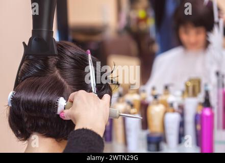 Die Friseurin trocknet ihr Haar als Brünette in einem Schönheitssalon. Stockfoto