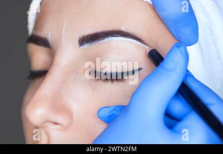 Permanent Make-up für Augenbrauen einer schönen Frau mit dicken Augenbrauen im Schönheitssalon. Nahaufnahme-Kosmetikerin, die Augenbrauen tätowiert. Stockfoto