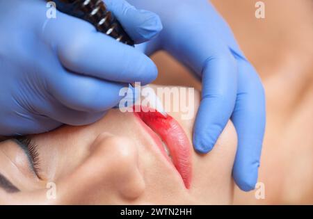 Permanentes Make-up für rote Lippen der schönen Frau im Schönheitssalon. Nahaufnahme-Kosmetikerin, die Lippen tätowiert. Stockfoto