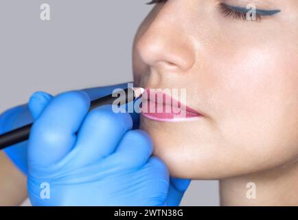 Permanentes Make-up für rote Lippen der schönen Frau im Schönheitssalon. Nahaufnahme-Kosmetikerin, die Lippen tätowiert. Stockfoto