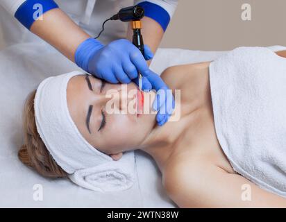 Permanentes Make-up für rote Lippen der schönen Frau im Schönheitssalon. Nahaufnahme-Kosmetikerin, die Lippen tätowiert. Stockfoto