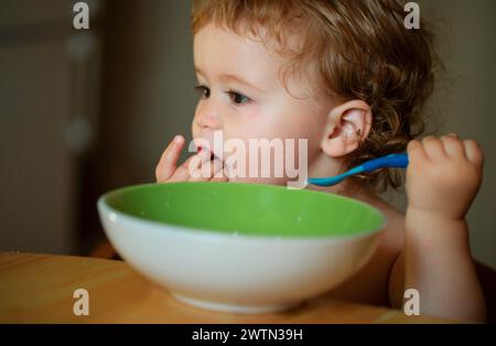 Lustige Baby Essen selbst mit einem Löffel in der Küche. Stockfoto