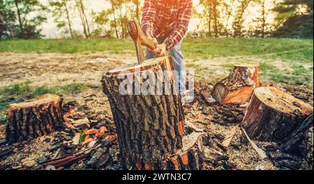 Männlicher Holzfäller im schwarz-roten karierten Hemd mit einer Axt, die im Wald einen Baum hackt. Stockfoto