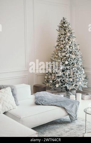 Weihnachtliche Einrichtung in einem Fotostudio in Grau und weiß. Schneeweißer Weihnachtsbaum, Geschenke und Laternen, Sofa. Unscharf. Platz für ein Fotoshooting Stockfoto