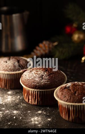 Schokoladenmuffins mit Puderzucker auf schwarzem Hintergrund. Weihnachtsdekoration. Stillleben aus nächster Nähe. Lebensmittelfoto Stockfoto