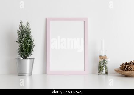Pinkfarbenes Rahmenmockup mit Zypresse, Kerzen und Tannenzapfen auf einem weißen Tisch. Weihnachtsdekoration. Stockfoto