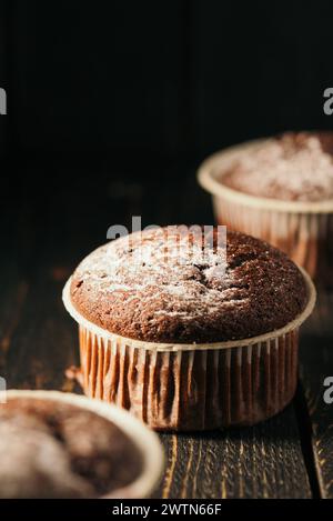 Schokoladenmuffins mit Puderzucker auf schwarzem Hintergrund. Stillleben aus nächster Nähe. Dunkel stimmungsvoll. Lebensmittelfoto Stockfoto
