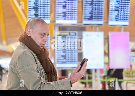 Überprüfen des Flugstatus: Ein Mann, der auf das Telefon blickt und Fluginformationen im Hintergrund angezeigt werden Stockfoto