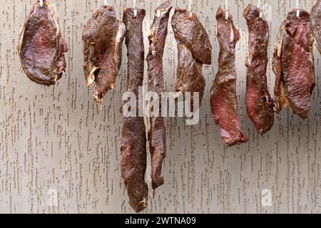 Rohe, gewürzte Rinderstücke hängen draußen zum Trocknen, um ein beliebtes südafrikanisches Gericht namens Biltong zu werden. Biltong ist ein gepökeltes Fleischprodukt. Stockfoto