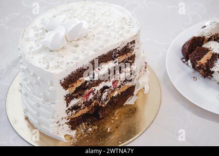 Weißer Partykuchen mit Perlen und weißer Glasur und roter Frucht- und Schokoladenfüllung, Kuchendesign. Handgemachter Kuchen für einen besonderen feierlichen Anlass. Stockfoto