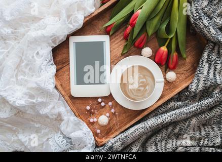 Romantische Komposition mit einer Tasse Kaffee, roten Tulpen und E-Reader mit Kopierraum auf Holztablett. Stockfoto