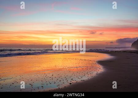 Atemberaubender goldener Sonnenuntergang, der die Sandküste ziert, den Himmel mit warmen Tönen übermalt und einen faszinierenden Glanz über dem ruhigen Strand wirft Stockfoto