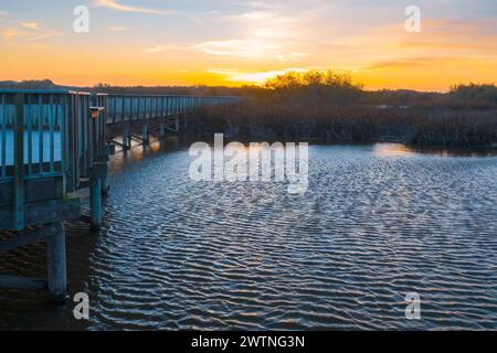See bei Sonnenuntergang, eine lange Holzpromenade durch den See und ein wunderschöner blau-goldener Himmel im Hintergrund, Kalifornien Stockfoto