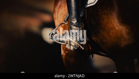 Abgebildet ist das Bein eines Reiters, der auf dem Rücken sitzt und ein Paar Reitstiefel mit Sporen trägt. Die Steigbügel sind sichtbar, die in Reitbetrieben verwendet werden Stockfoto