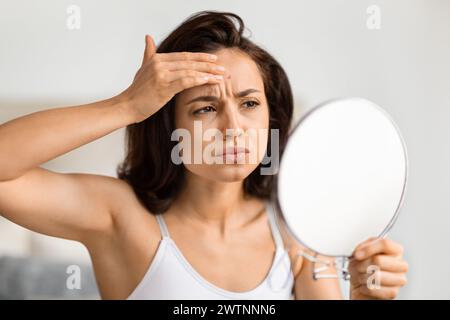 Verärgerte Millennial-Frau, die in den Spiegel blickt und Pickel überprüft Stockfoto