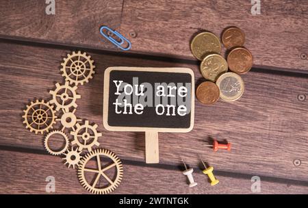 Ein Mann hält ein Stück Papier, das sagt: „Du bist der eine“. Das Papier ist weiß mit schwarzen handgeschriebenen Buchstaben und der Hintergrund ist rot. Stockfoto