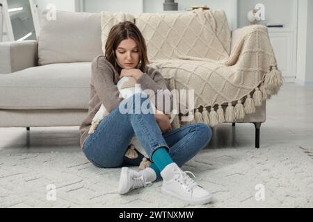 Traurige junge Frau, die zu Hause auf dem Boden sitzt Stockfoto