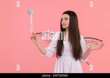 Schönes Mädchen im Feenkostüm mit Flügeln und Zauberstab auf rosa Hintergrund Stockfoto