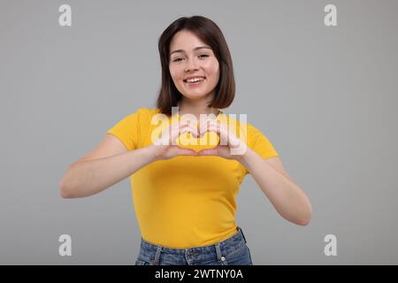 Glückliche Frau, die Herzgeste mit Händen auf grauem Hintergrund zeigt Stockfoto