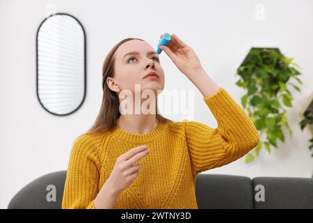 Junge Frau, die drinnen medizinische Augentropfen aufträgt Stockfoto