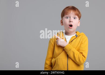 Ein überraschter kleiner Junge, der auf etwas auf grauem Hintergrund zeigt, Platz für Text Stockfoto