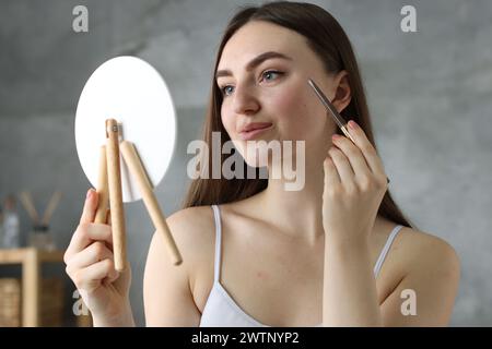 Schöne Frau, die Sommersprossen mit Stift vor dem kleinen Spiegel im Haus zeichnet Stockfoto