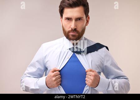 Selbstbewusster Geschäftsmann, der ein Superheldenkostüm unter dem Anzug auf beigefarbenem Hintergrund trägt Stockfoto