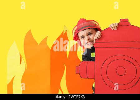 Netter kleiner Feuerwehrmann mit Papierhydrant und Flamme auf gelbem Hintergrund Stockfoto