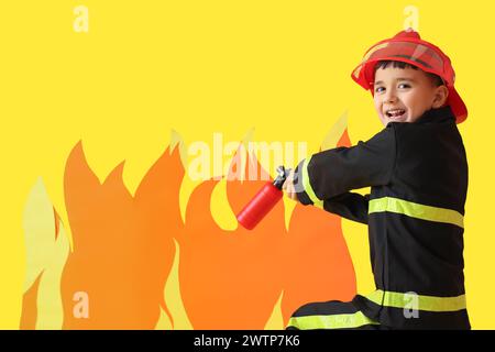 Niedliche kleine Feuerwehrmann löscht Papierflamme auf gelbem Hintergrund Stockfoto