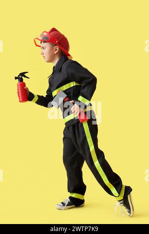 Niedlicher kleiner Feuerwehrmann mit Spielzeugwerkzeugen auf gelbem Hintergrund Stockfoto